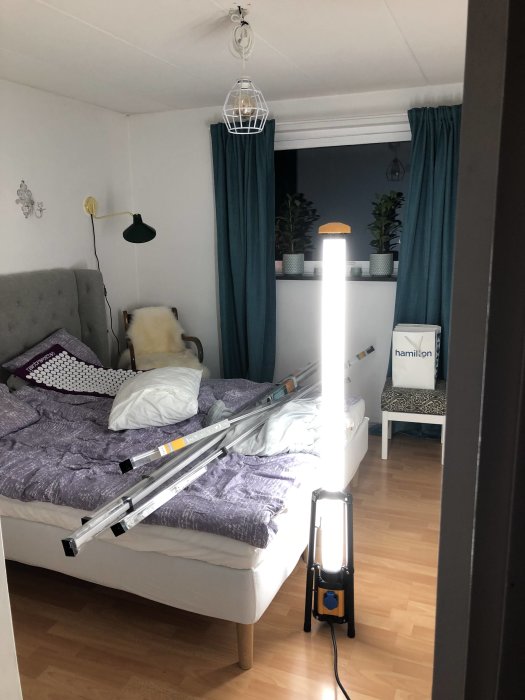 Ett sovrum med en ny arbetsbelysning tänd på golvet och byggmaterial på sängen, indikerar förberedelser för inomhusprojekt.