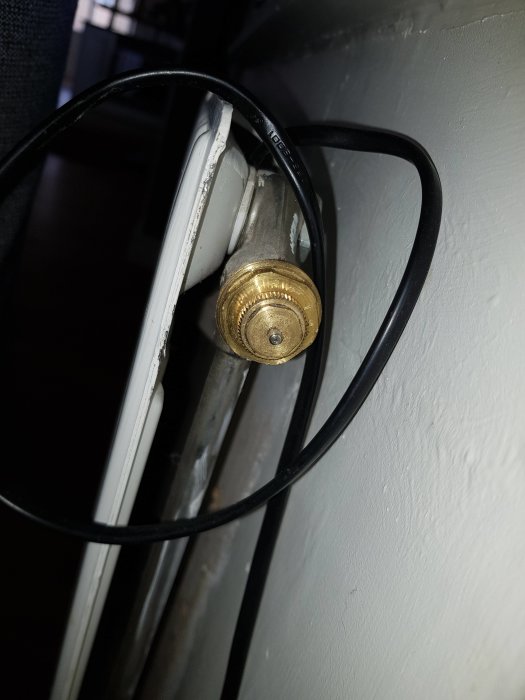 Räfflat, runt radiatorvred monterat på rör med en svart kabel runtomkring.