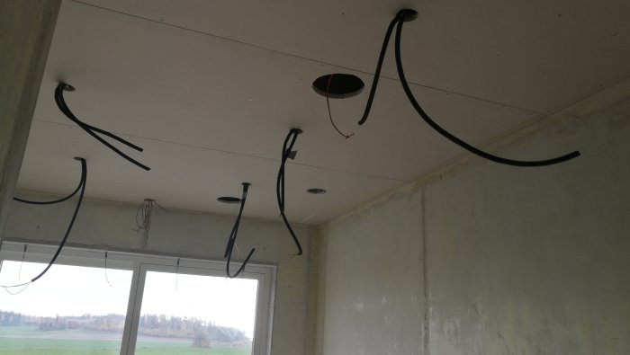 Installation av takhögtalare med synliga kablar och uttag i ett oinrett rum.