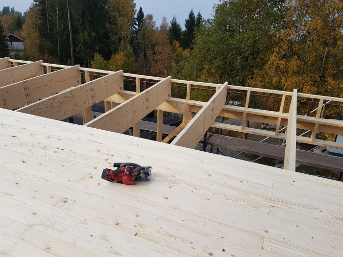 Nyinstallerat råsponttak med synliga balkar och en batteridriven skruvdragare på förgrunden, omgivet av träd.