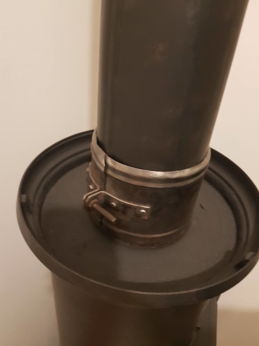 Detaljbild av överdelen på en svart vedspis med synlig rökrörsanslutning och spjäll.