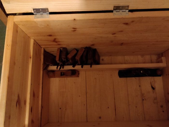 Trähyvlar upphängda på väggen i en träverkstad, med ett 2x4 virkesstycke på golvet.
