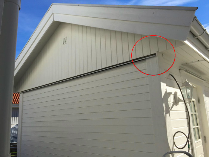 Detaljbild av en vit husknut med markerad springa där tak möter vägg som kan läcka in vatten.