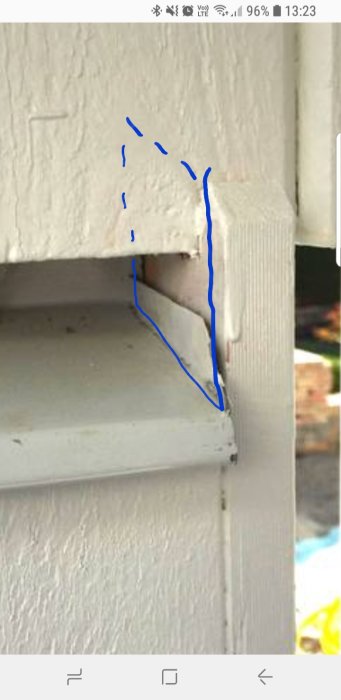Skadad hörnkant på vitmålad husvägg med blå streck som markerar förslag till reparation.