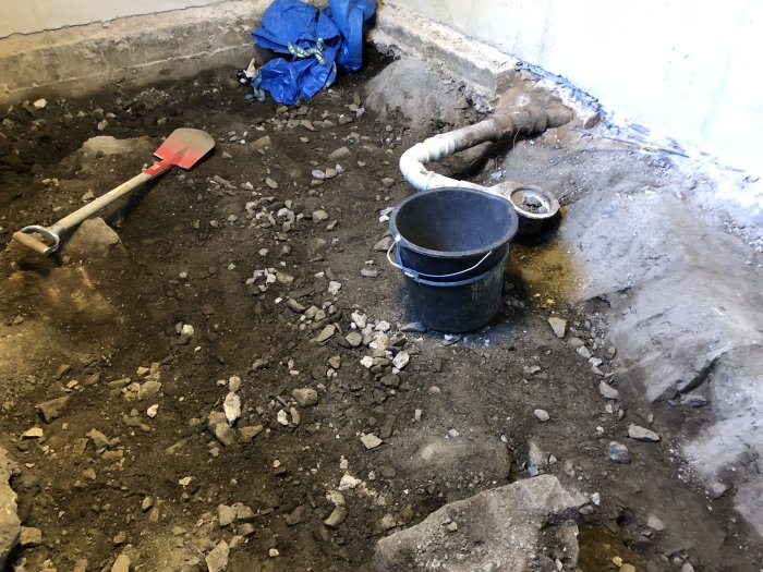 Uppgrävning i källarrum med synligt berg och byggverktyg, förberedelse för gjutning av en ny platta med golvvärme.