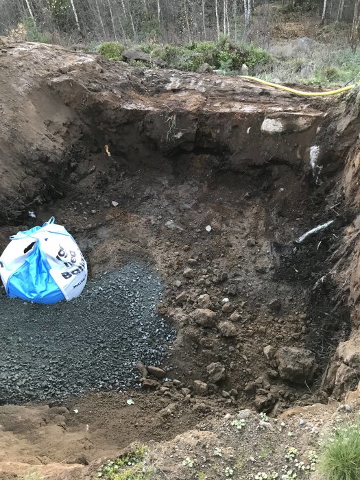 Ett stort, urgrävt hål i marken med grus i ena hörnet och en grus-säck, omgivet av skog.