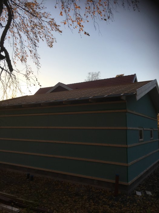 Garage under renovering med nymålade fasadbräder och delvis påsatt panel, höstlöv i förgrunden.