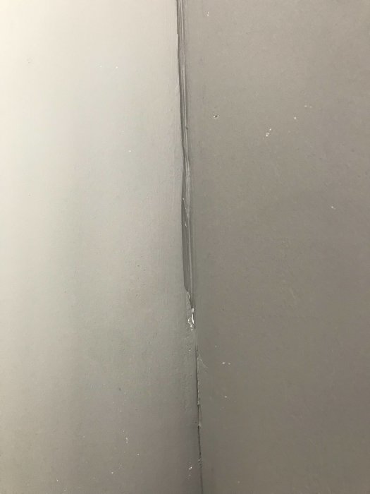 Köksstomme med damm i glipan bredvid vägg, fastskruvad golvsockel, utan plastskydd.