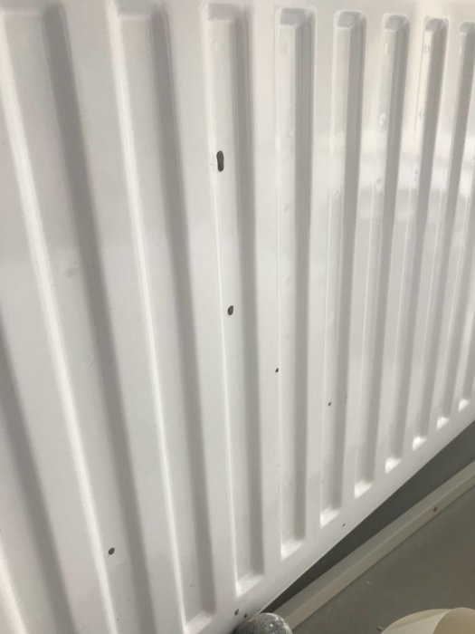 Vit nyinstallerad radiator med spår av färg och spackel, vilket indikerar brist på skydd under renovering.