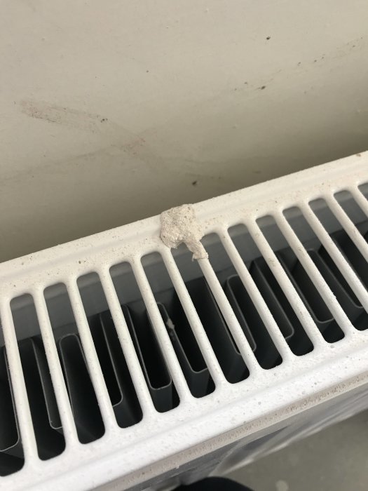 Nyinstallerad vit radiator med spackel och damm ovanpå, ojämnheter synliga på vägg bakom.