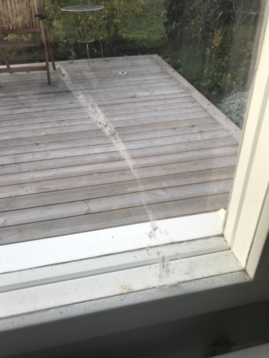 Fotsavtryck och damm syns på en vit fönsterkarm med utsikt över en trädgård och däck.