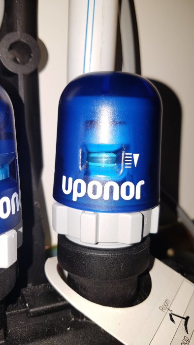 Blå Uponor-termostatventil med synlig indikator och sträckmarkeringar, monterad på en vit vattenledning.