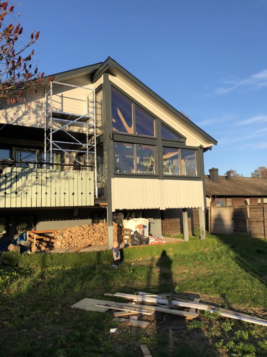 Husfasad med stora fönster och en delvis rivet byggställning i solljus, samt planerad ingång för katt.