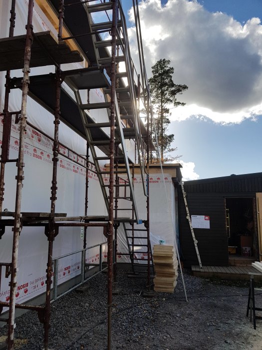 Byggnadsställningar vid hus med nyinstallerad vindpapp och isoleringsmaterial på marken.