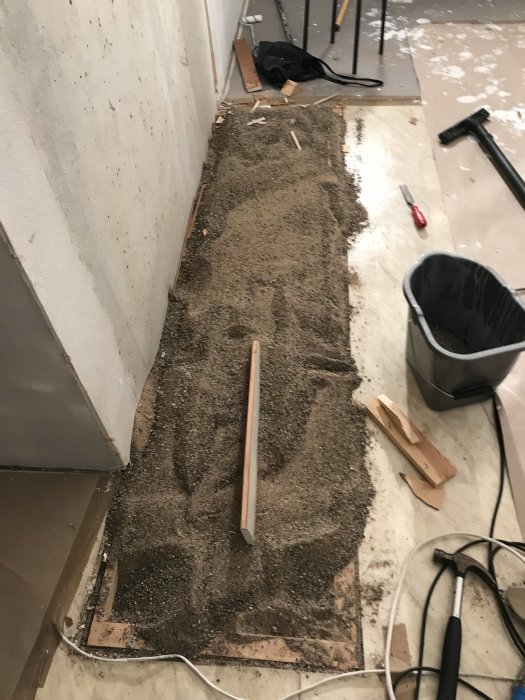 Hål i lägenhetsgolv under renovering med synligt underlag av sand, plast, golvspån och träreglar.