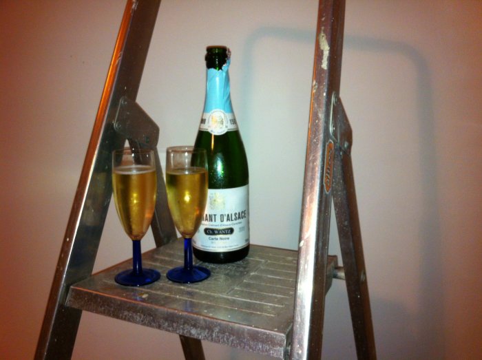 Två champagneglas och en öppnad flaska på en stege i ett nyligen renoverat utrymme.