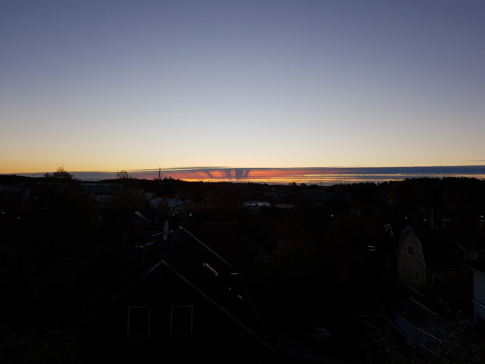 Soluppgång med silhuett av en stad och reflekterande ljus över vatten.