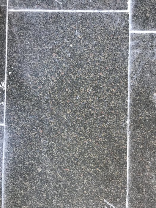 Närbild på en granitplatta med synlig textur och små inslag av gipsdamm.