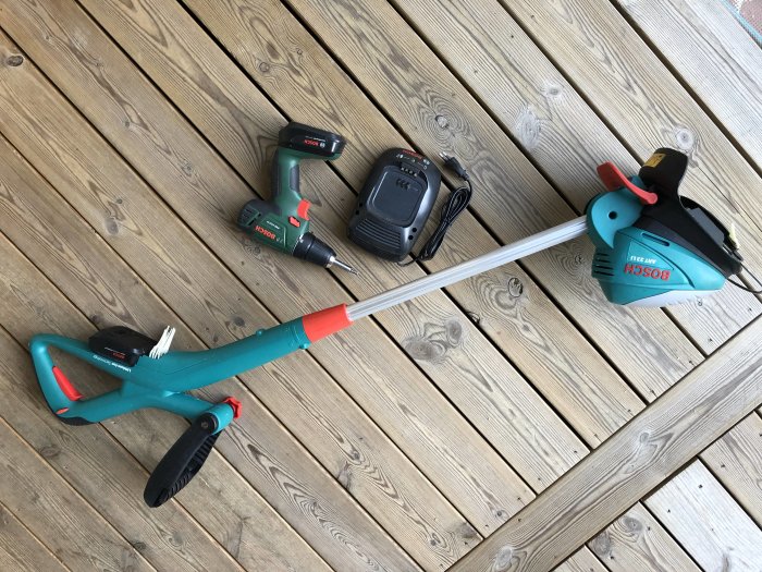 Batteridriven grästrimmer med justerbart skaft, två batterier och laddare på ett trägolv. Skruvdragaren ingår inte.