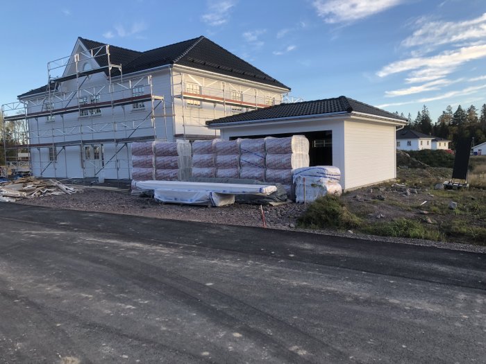 Hus under renovering med byggnadsställningar och isoleringsmaterial staplat utanför.