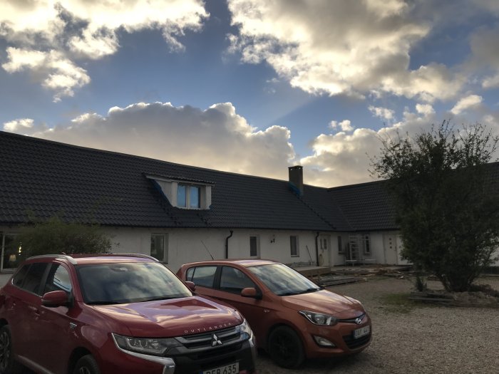 Nyrenoverat hustak med en takkupa och skorsten, omgivet av en del byggmaterial och två bilar framför huset.