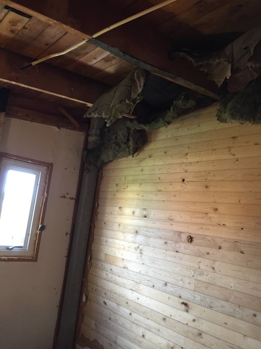 Renoveringsarbete i badrum med synliga takbjälkar och luckor i isoleringsmaterialet mot snedtak av trä.