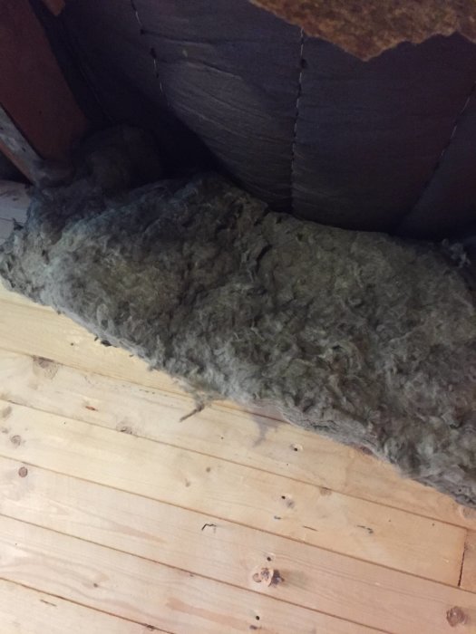 Isoleringsmatta fästad vid takbjälkar med träbitar för att skapa luftspalt i byggprojekt.