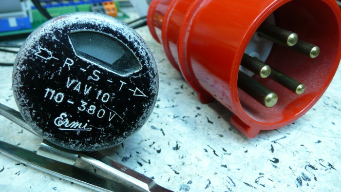 Retro fasföljdsvisare med svart streck för fasföljden, bredvid en röd trefasmotoranslutningskontakt.