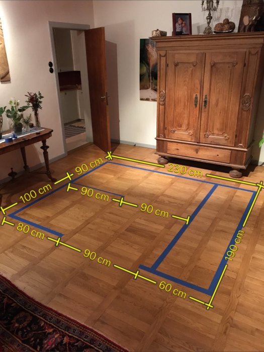 En tejpad uppställning på ett trägolv markerar dimensionerna för ett framtida badrum med mätningar.