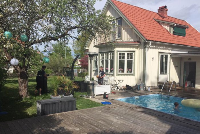 Familj förbereder renovering i trädgård vid gammal villa med pool och grönska.