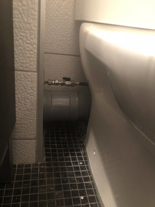 Rörgenomföring i ett trångt utrymme bakom en toalett med synlig märkning.