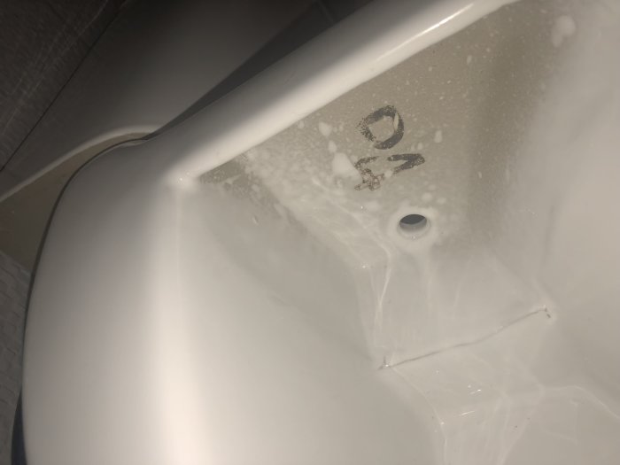Närbild på undersidan av en vit stol med en suddig märkning, möjligtvis "P4" eller "B4", och skumrester.