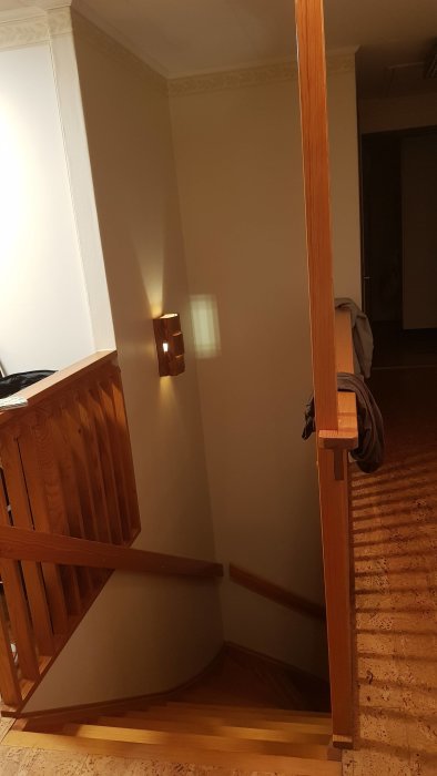 En tom trappvägg med träledstänger och ett väggmonterat ljus, potential för en stor konstinstallation.