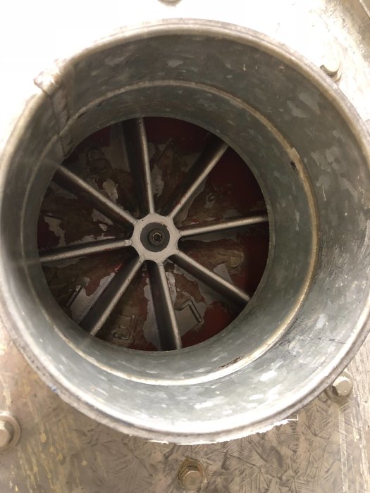 Inuti en spånsug med en gammal impeller med raka blad, synlig genom öppningen av metallhöljet.