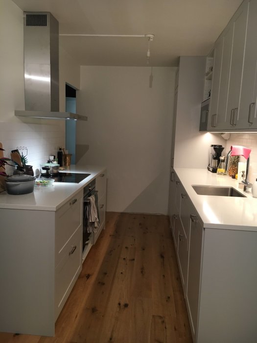 Kök efter renovering med vita skåp, rostfri fläkt och trägolv.