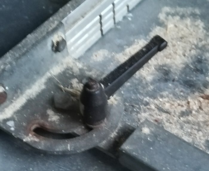 Närbild av ett söndergånget svart handtag på en såg, omgivet av sågspån.