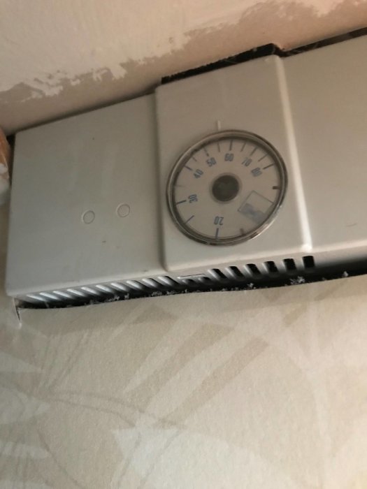 Hygrostat med analog fuktmätare på en vägg, närbild på mätare och inställningsknappar.