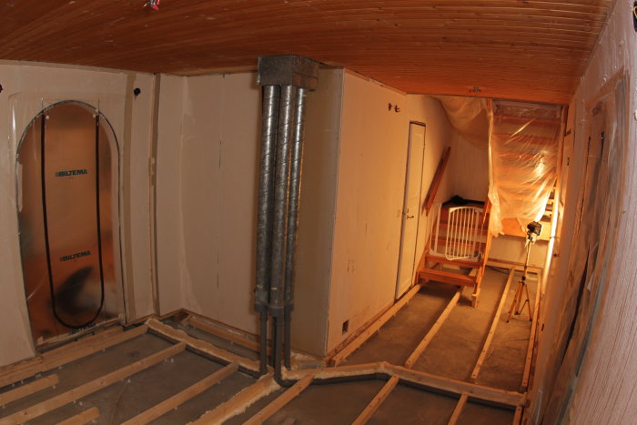 Interiör av ett hus under renovering med öppet golv och synliga ventilationsschakt.