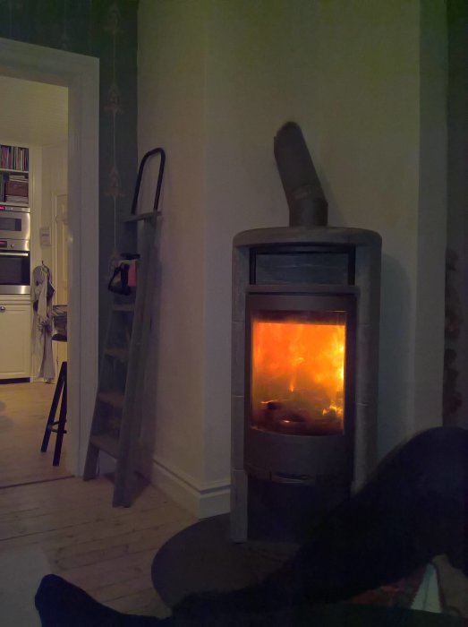 Brinnande ved i en Contura-kamin med synliga rör och murstock, i ett hemmiljö.