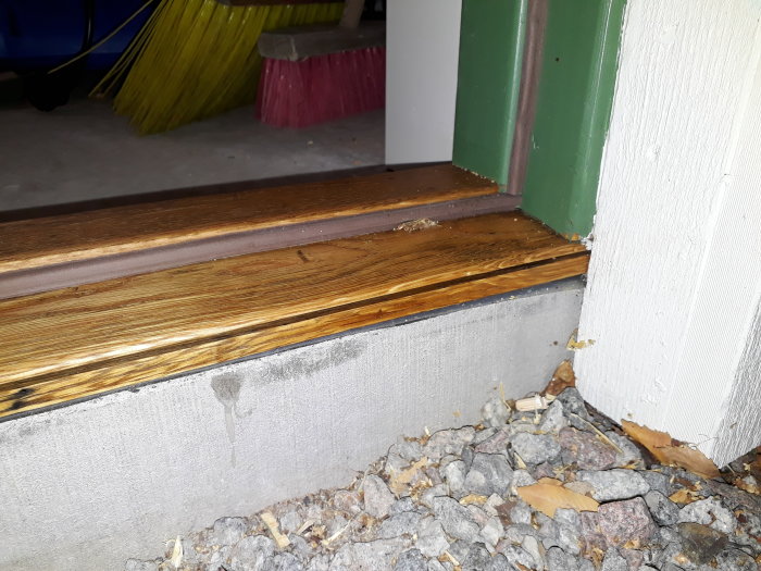 Egentillverkad dörrkarm med uppsågat spår för tröskelplåt, stenar och kvistar på marken.