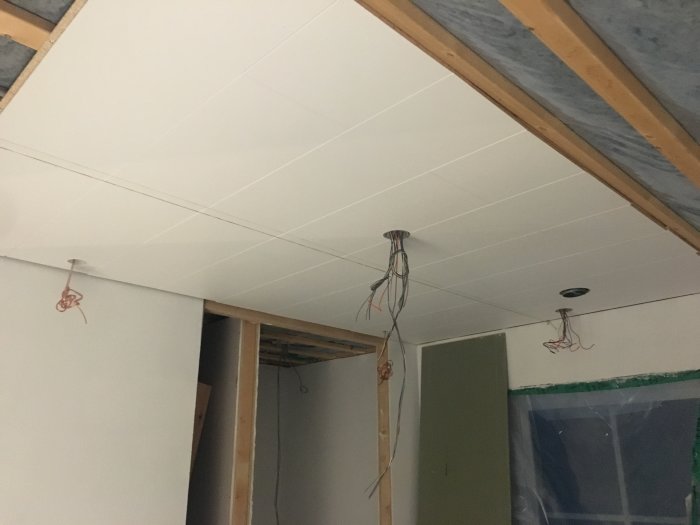 Innertak under installation med vita plattor som ser sneda ut, osynlig laser, exponerade takbjälkar och -kablar.