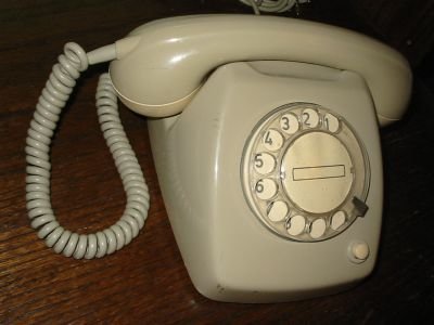 Gammal beige roterande telefon från holländska postverket på ett mörkt bord.