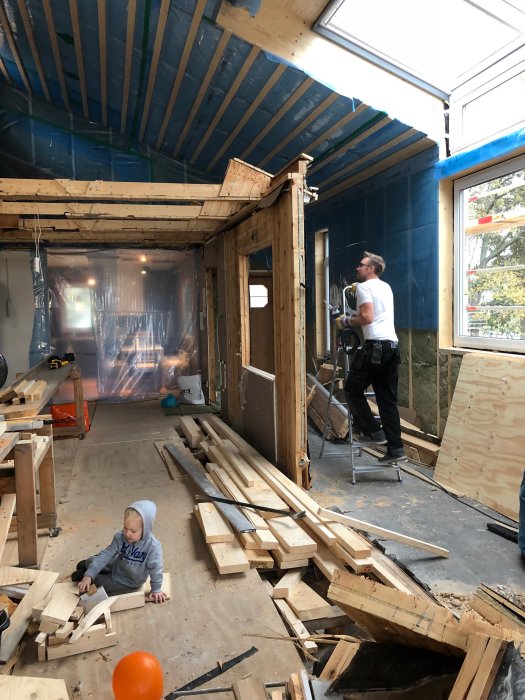 Renoveringsarbete inomhus med isolerat blått tak, träkonstruktion och barn på golvet.