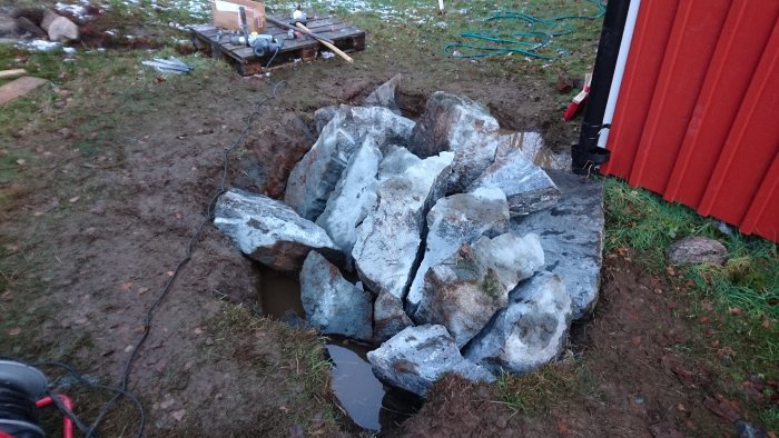 Stora stenbumlingar vid en stuga, redo att klyvas för lyftning, med borrutrustning nära.