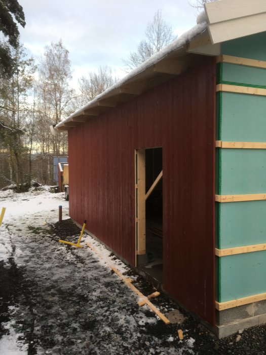 Nypanelat garage med snö på taket och snöfläckar på marken.