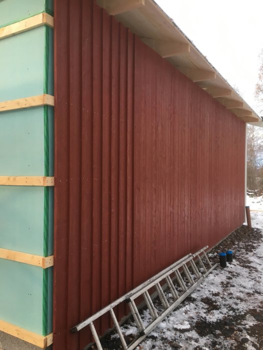 Nyinstallerad röd panel på en garagesida med snö på marken och en stege lutad mot väggen.