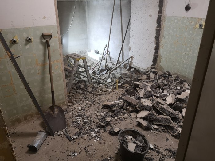 Rivningsarbete inomhus med betongspill, en spade och en kanalfläkt i ett dammigt rum.