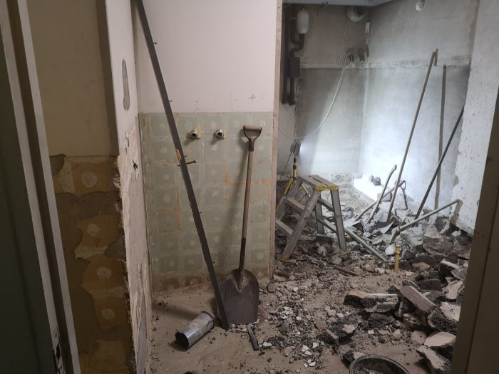 Rivningsarbete inuti byggnad, med synlig sten och bråte på golvet samt en kanalfläkt och verktyg.