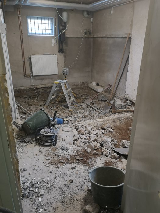 Ett rum under rivning med betongspill, en stege, verktyg och ventilation.