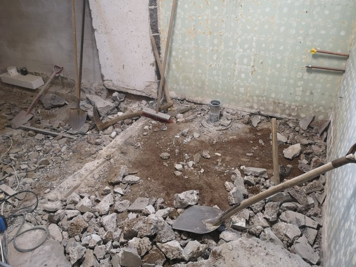 Rivningsarbete i rum med utsprängt berg och byggverktyg, bredvid ett expansionskärl och ventilationsslang.